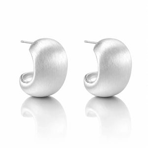 A pair of matte silver crescent-shaped hoop earrings with post backs, displayed on a clean white reflective surface.