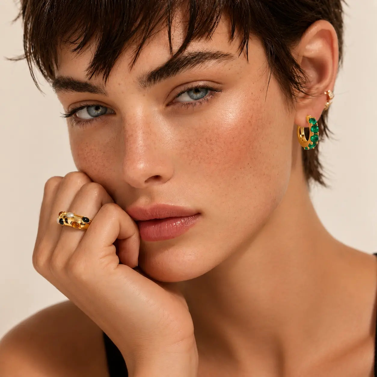 Close-up of a woman wearing gold earrings and ring against a beige background