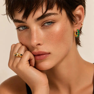 Close-up of a woman wearing gold earrings and ring against a beige background