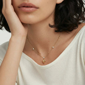 Woman wearing a delicate gold necklace with a heart pendant.
