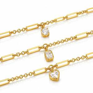 Three gold chain bracelets with rectangular bar links, each featuring a clear gemstone charm in a different shape: oval, emerald, and heart, displayed on a white background.