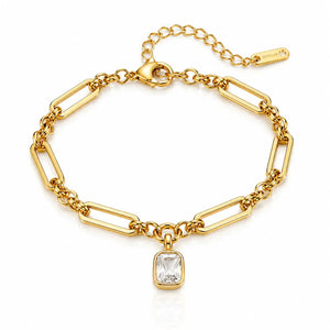 A gold paperclip chain bracelet with a rectangular clear gemstone pendant, displayed on a clean white background with a subtle reflection.