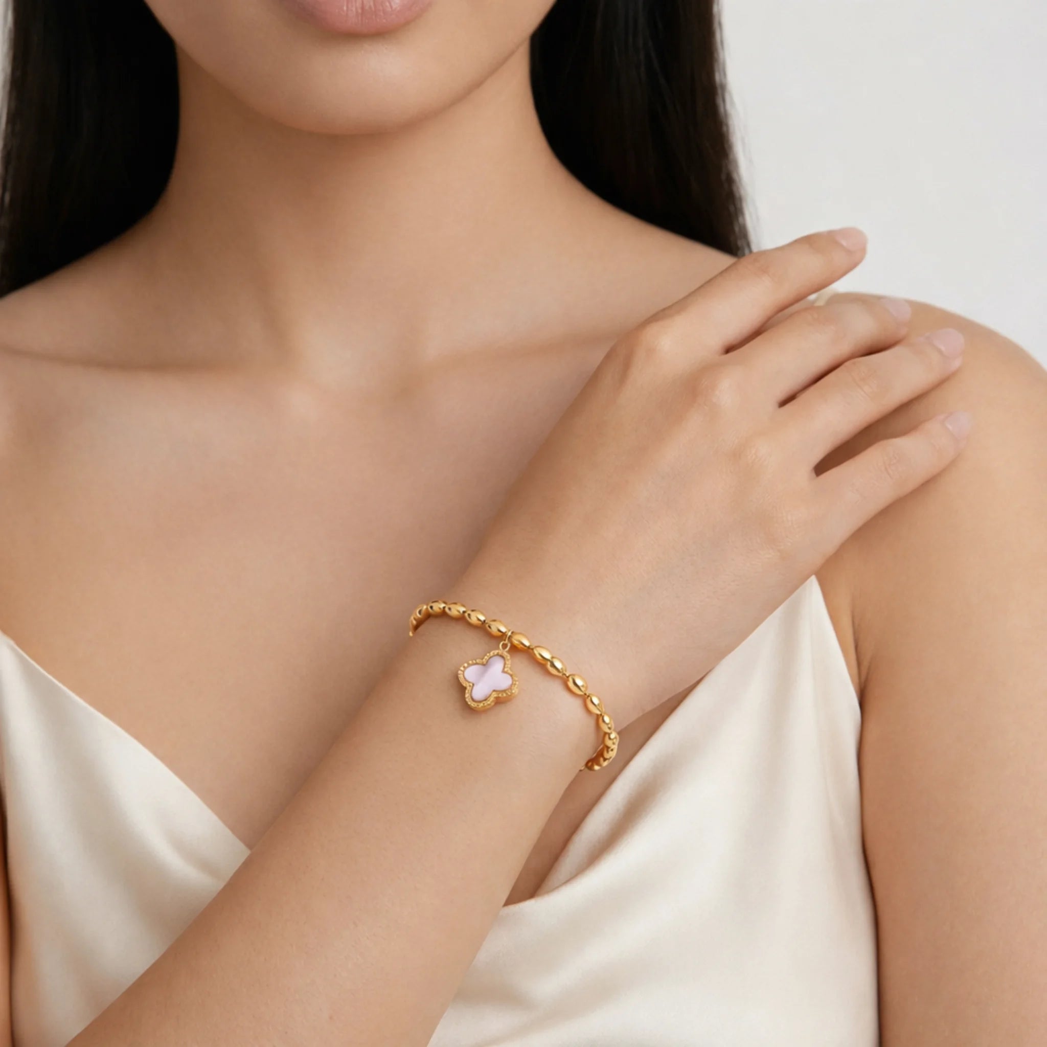 Close-up of a woman's arm wearing a gold bracelet with a floral charm on a plain background
