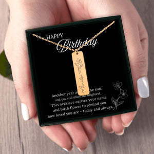 Gold necklace with a pendant on a 'Happy Birthday' card held by a hand.