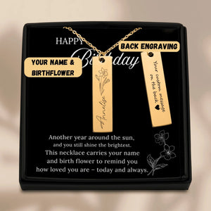 Gold necklace with engraved name and birthflower in a black gift box.