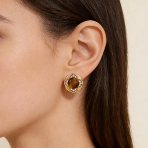 Woman wearing a gold stud earring with tiger's eye gemstone and crystal accents