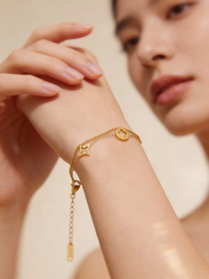 Gold bracelet with star and heart charms on a person's wrist against a neutral background
