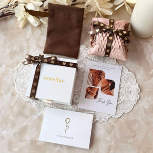 Jewelry packaging set with brown pouch, pink box, and cards on a lace doily.