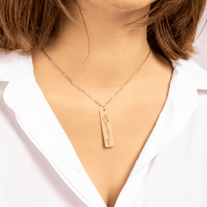 Gold rectangular pendant necklace with flower engraving and name 'Amelie' worn with white shirt