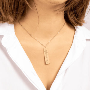 Gold rectangular pendant necklace with flower engraving and name 'Amelie' worn with white shirt
