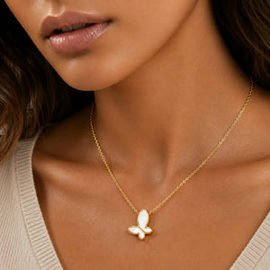 A close-up of a model wearing a delicate gold chain necklace with a small butterfly pendant featuring white inlay details.