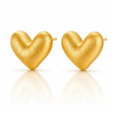 A pair of textured gold heart-shaped stud earrings on a clean white background with soft reflections below.