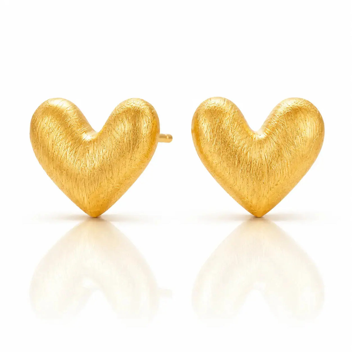 A pair of textured gold heart stud earrings on a clean white background with soft reflections below.
