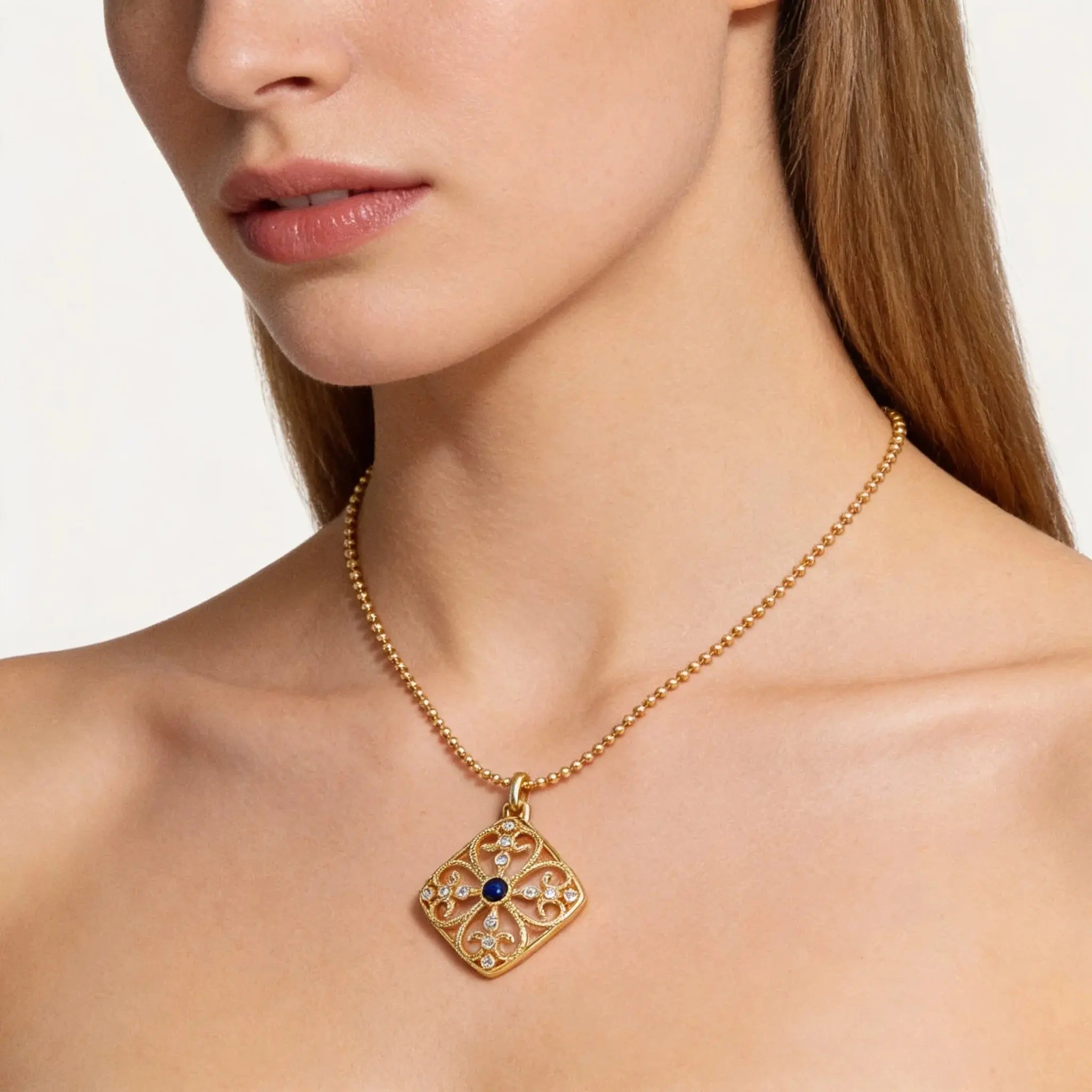 Gold necklace with a decorative pendant worn by a model on a neutral background