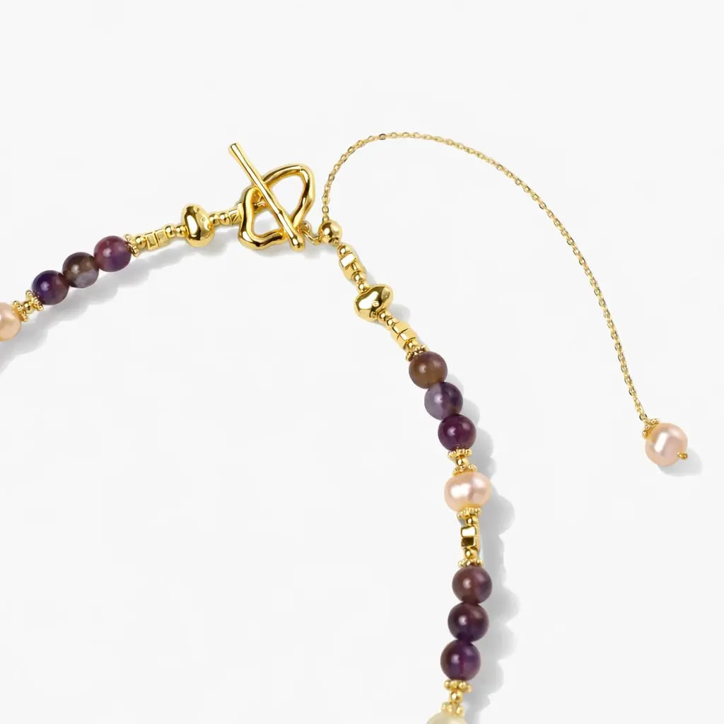 Gold amethyst and pearl necklace with decorative clasp and adjustable chain on white background