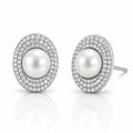 A pair of oval stud earrings featuring a central white pearl surrounded by double rows of small clear pavé stones in a silver-toned setting, shown on a white reflective background.