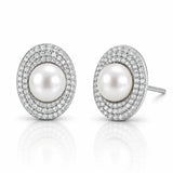A pair of oval stud earrings featuring a central white pearl surrounded by double rows of small clear pavé stones in a silver-toned setting, shown on a white reflective background.