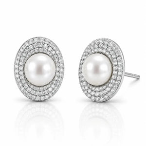 A pair of oval stud earrings featuring a central white pearl surrounded by double rows of small clear pavé stones in a silver-toned setting, shown on a white reflective background.