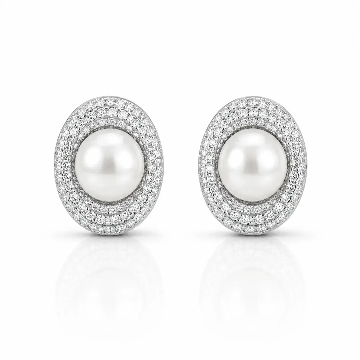 A pair of oval stud earrings featuring a central white pearl surrounded by a halo of small clear stones in a silver-toned setting, shown on a clean white background with a soft reflection below.
