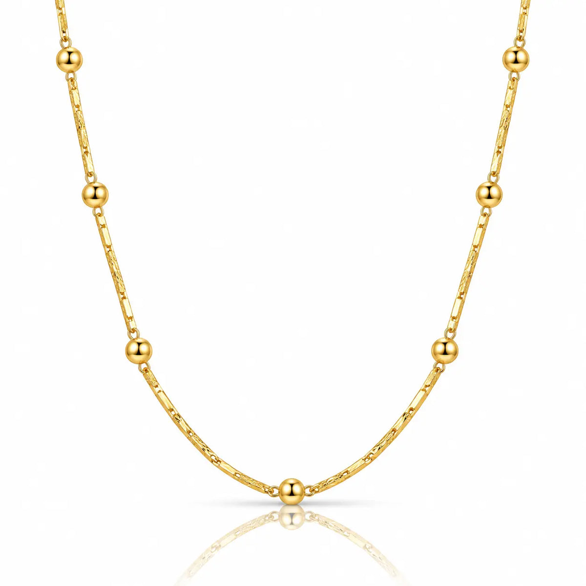 A delicate gold chain necklace featuring alternating small spherical beads and elongated oval links, displayed on a clean white background with a soft reflection below.