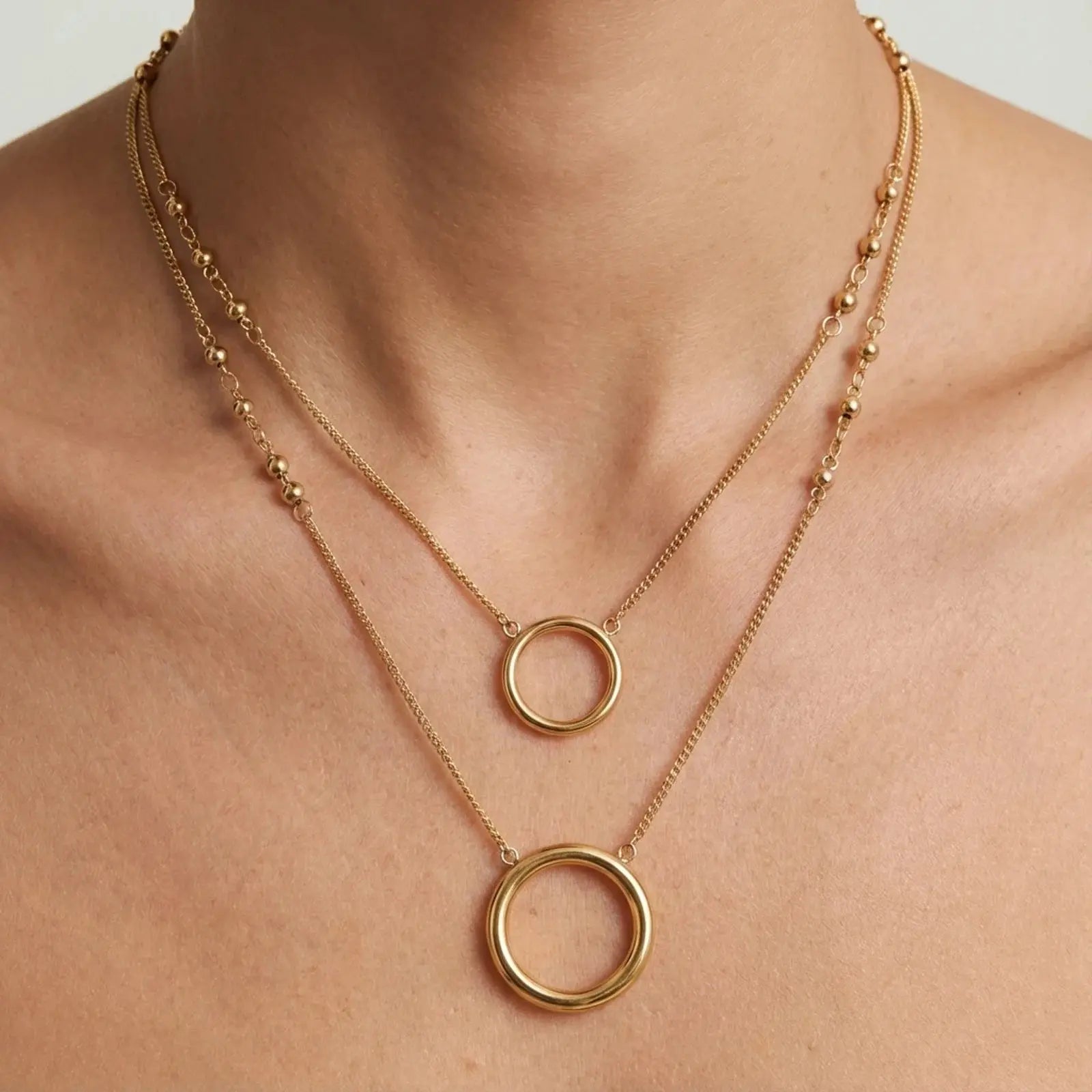 Gold necklace with circular pendants on a person's neck against a neutral background