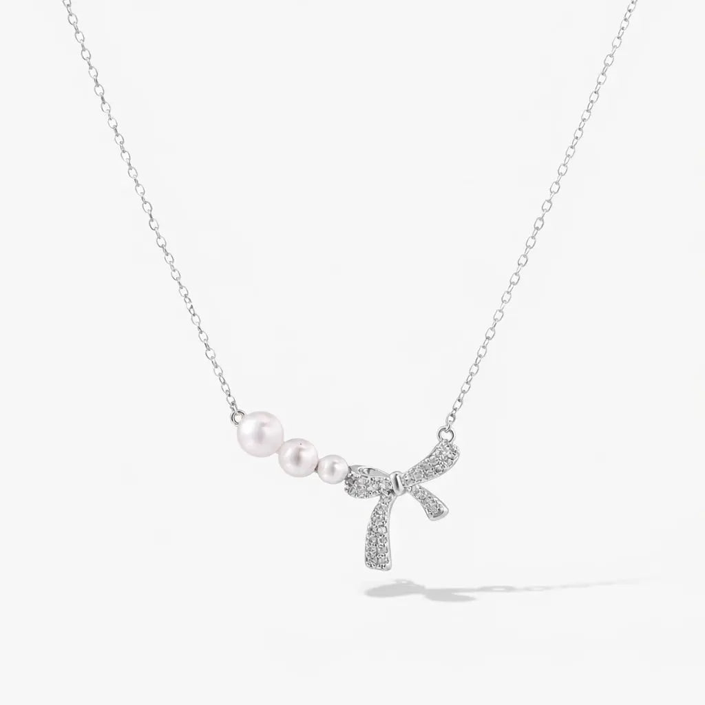 Silver necklace with three pearls and a crystal-studded bow pendant on a white background