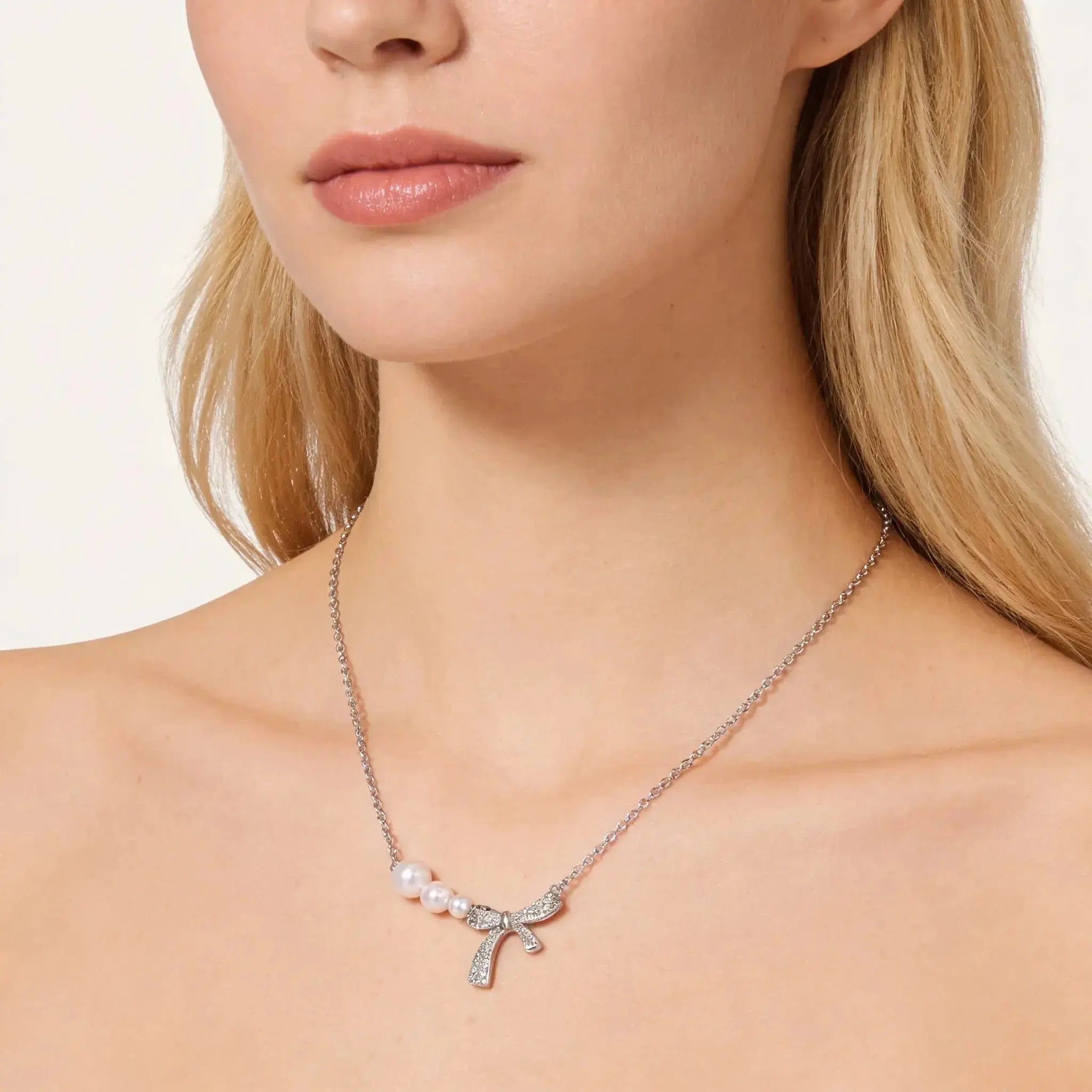 Necklace with a bow and pearl detail worn by a model on a plain background