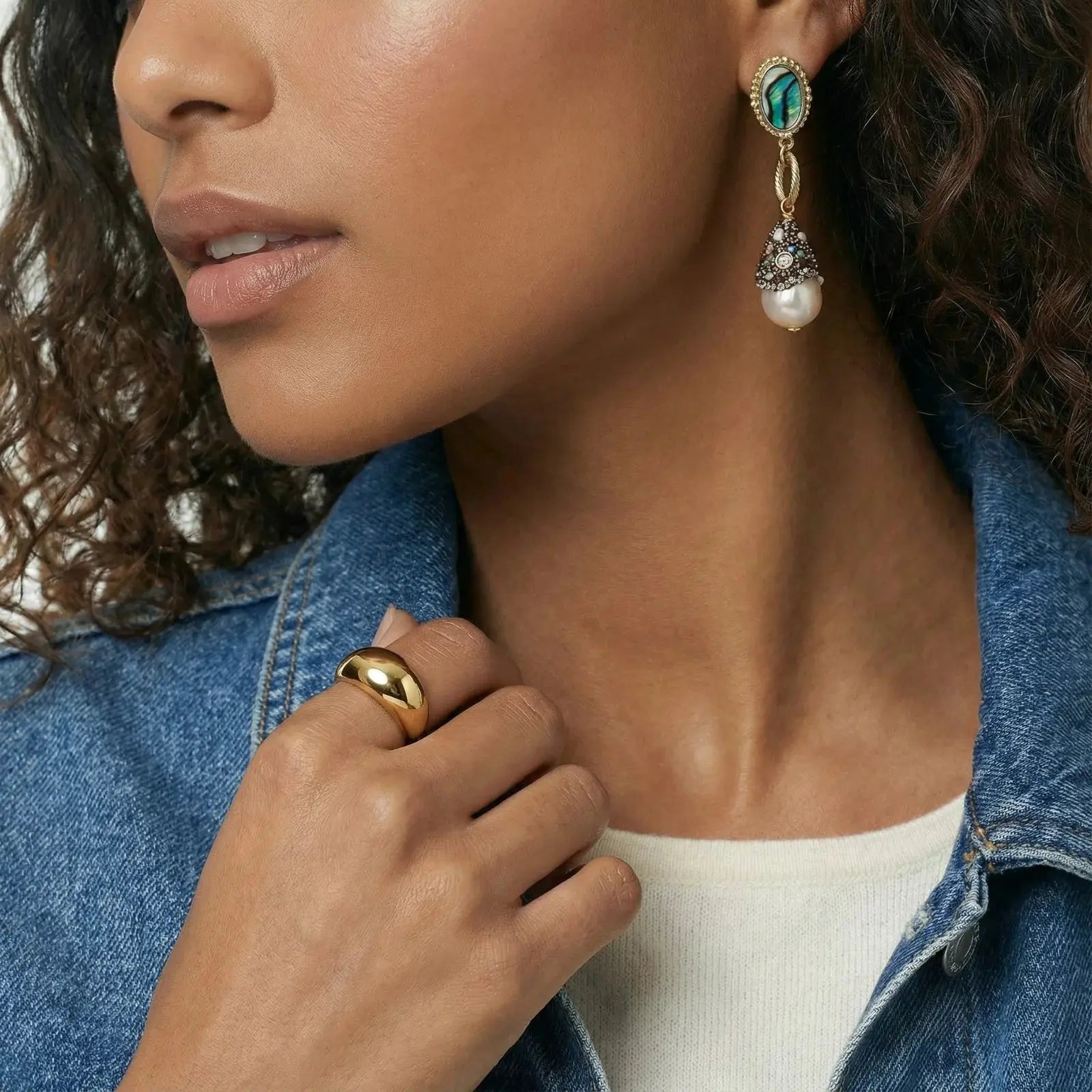 Woman wearing baroque pearl drop earrings with abalone detail and gold band ring