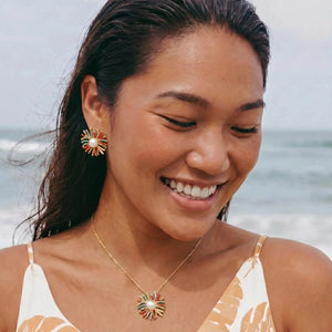 Woman on a beach wearing a necklace and earrings with a blurred ocean background