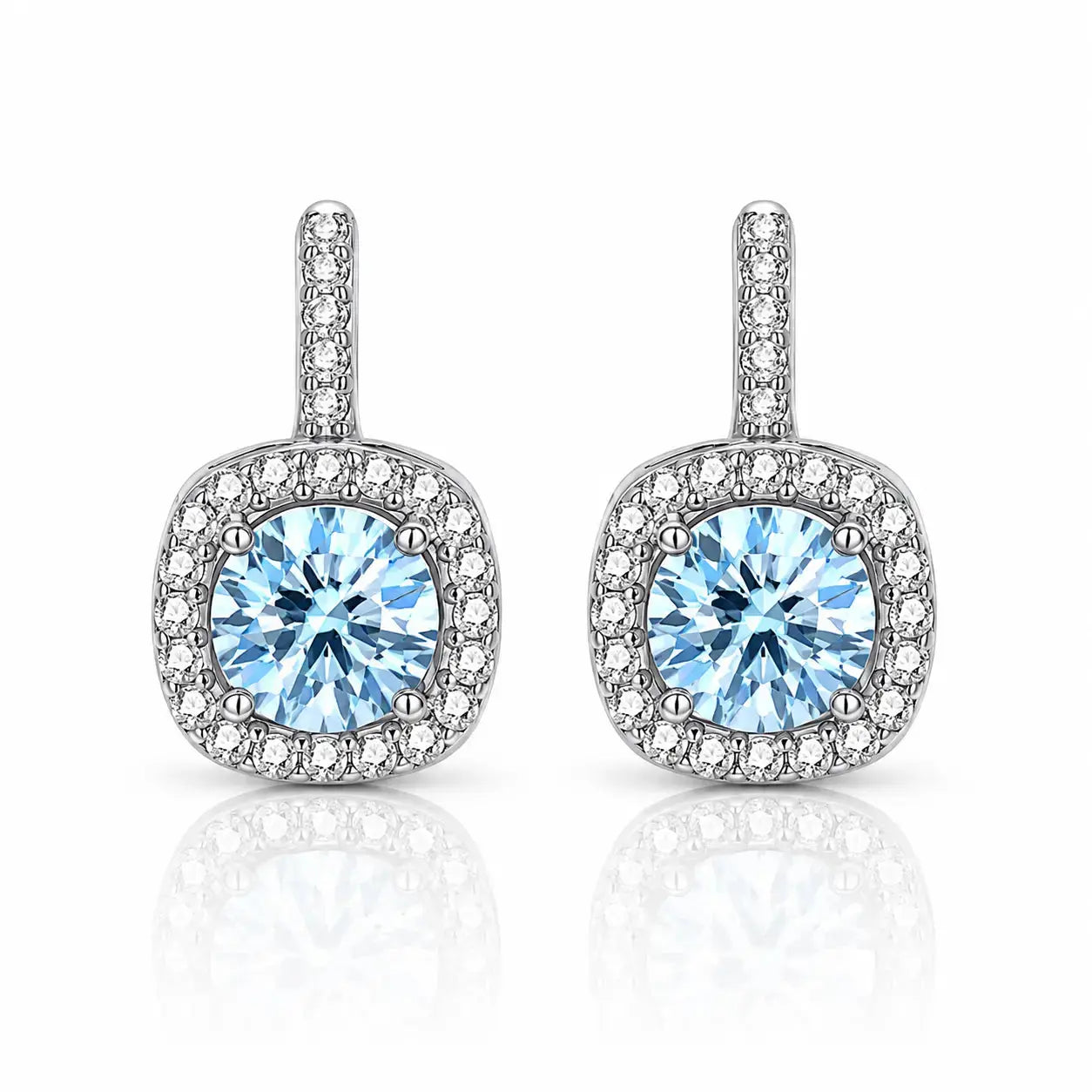 A pair of silver-toned halo stud earrings featuring a round light blue center stone surrounded by a halo of small clear stones, set against a white background with a soft reflection below.