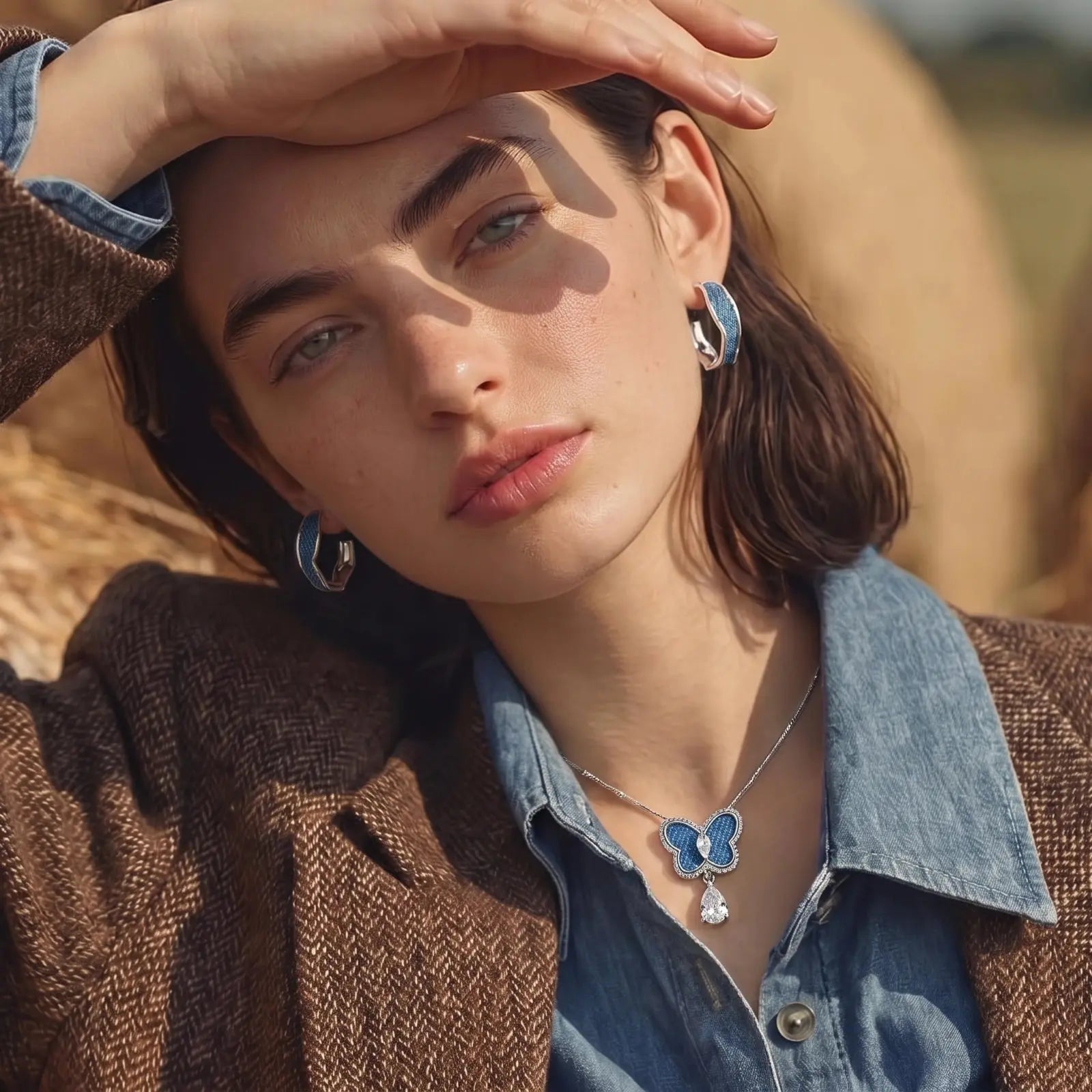 Woman wearing a brown coat and blue shirt with jewelry, sunlit outdoors