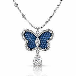A silver butterfly pendant necklace with deep blue pavé inlay and clear teardrop gemstones, shown on a white background with a soft reflection.