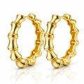 A pair of gold hoop earrings with a polished bamboo-inspired segmented design, displayed on a clean white background with a soft reflection below.