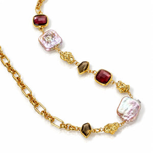 A gold chain necklace featuring alternating square-cut dark red gemstones, baroque-style iridescent pearl-like beads, and textured gold spacer details, displayed on a clean white background.