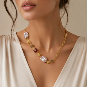 A gold chain necklace with irregular white and red gemstone accents, worn by a model in a cream-colored blouse against a warm beige background.