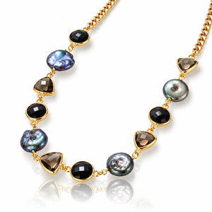 A gold-tone beaded necklace featuring natural baroque pearls and smoky triangular beads, displayed on a clean white background with a soft reflection.