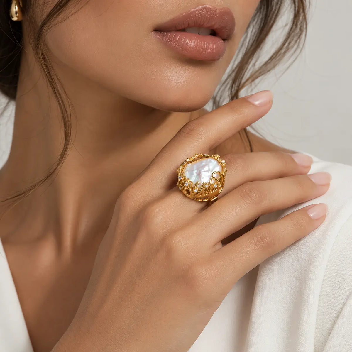 A close-up lifestyle shot of a model wearing a gold ring with a large, textured white mother-of-pearl cabochon on her finger.