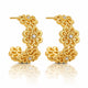 A pair of gold huggie hoop earrings with intricate floral filigree detailing and small clear crystal accents, displayed on a clean white background with a soft reflection below.