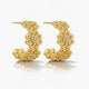 Gold filigree hoop earrings with floral design and small clear stones on white background