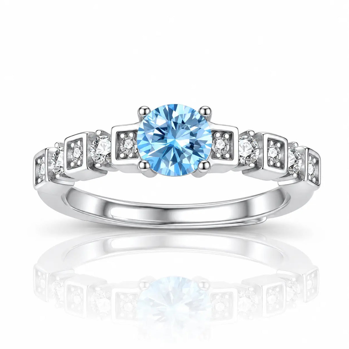 A silver-toned diamond ring featuring a round-cut light blue center stone and small clear accent stones set in square-shaped bands, shown on a white background with a soft reflection below.
