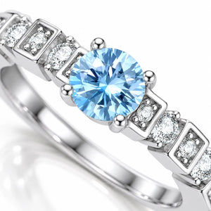 A close-up shot of a silver-toned ring featuring a large round light blue center stone and smaller clear accent stones set in a square pattern along the band, shown on a clean white background.