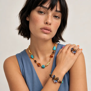 A gold chain necklace featuring turquoise, amber, and dark brown beads, displayed on a clean white background with a soft reflection.