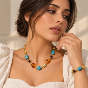 A gold chain necklace featuring turquoise, amber, and dark brown beads, displayed on a clean white background with a soft reflection.