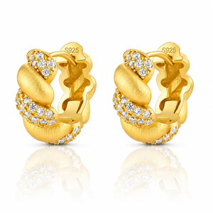 A pair of gold huggie hoop earrings with clear pavé-set round stones, shown on a white background with a soft reflection below. The inside of the earrings is stamped with 'S925' indicating sterling silver base metal.