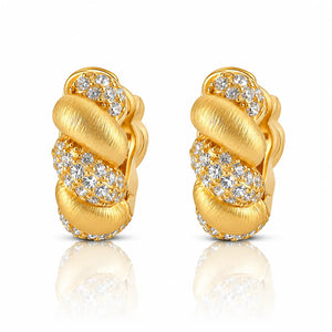 A pair of gold huggie hoop earrings with textured brushed gold bands and pavé-set clear stones, shown on a white background with a soft reflection below.