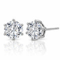 A pair of round-cut diamond stud earrings in a silver four-prong setting, with one earring facing forward and the other angled to show the post and back, on a reflective white surface.