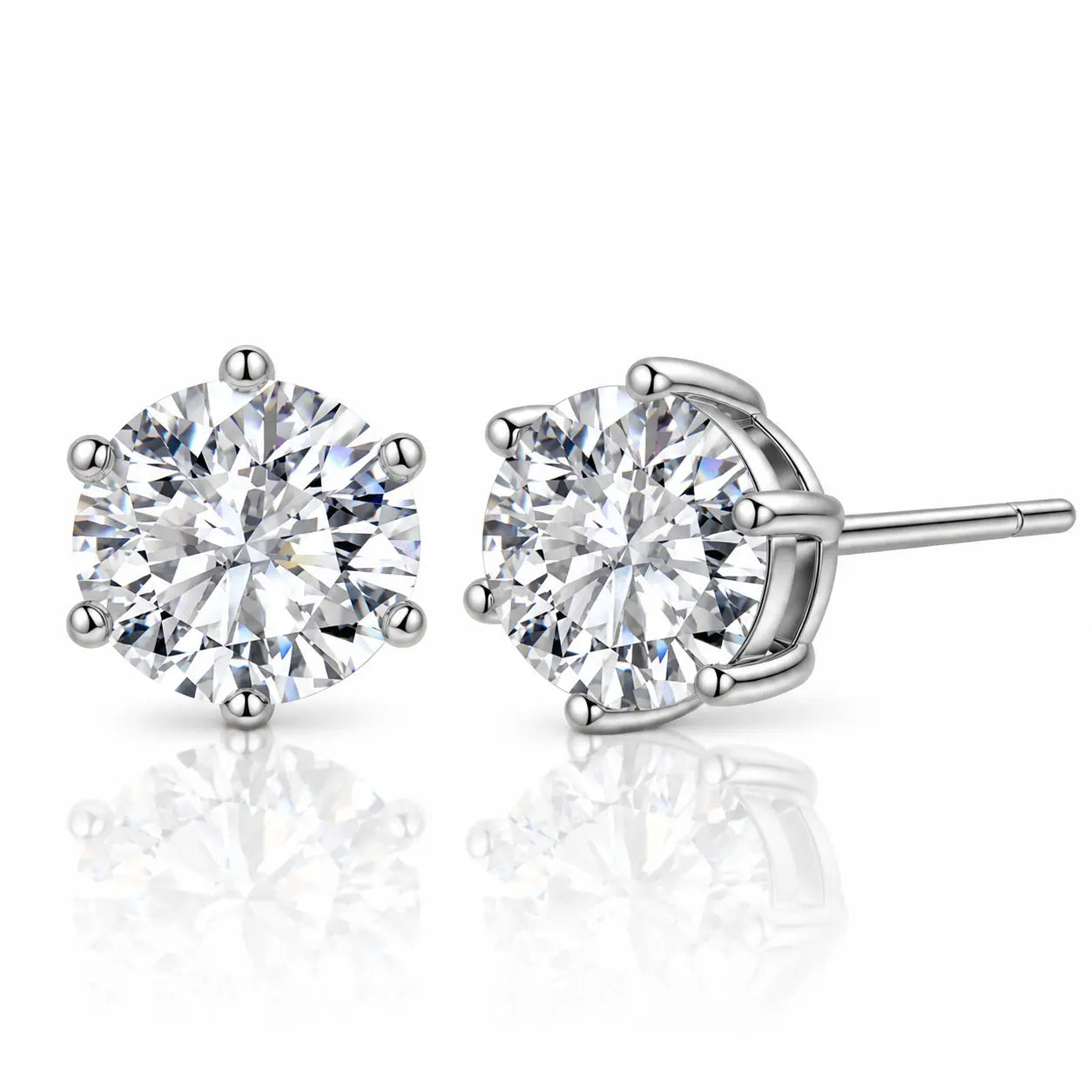 A pair of round-cut diamond stud earrings in a silver four-prong setting, with one earring facing forward and the other angled to show the post and back, on a reflective white surface.