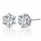 A pair of round-cut diamond stud earrings in a silver four-prong setting, with one earring facing forward and the other angled to show the post and back, on a reflective white surface.