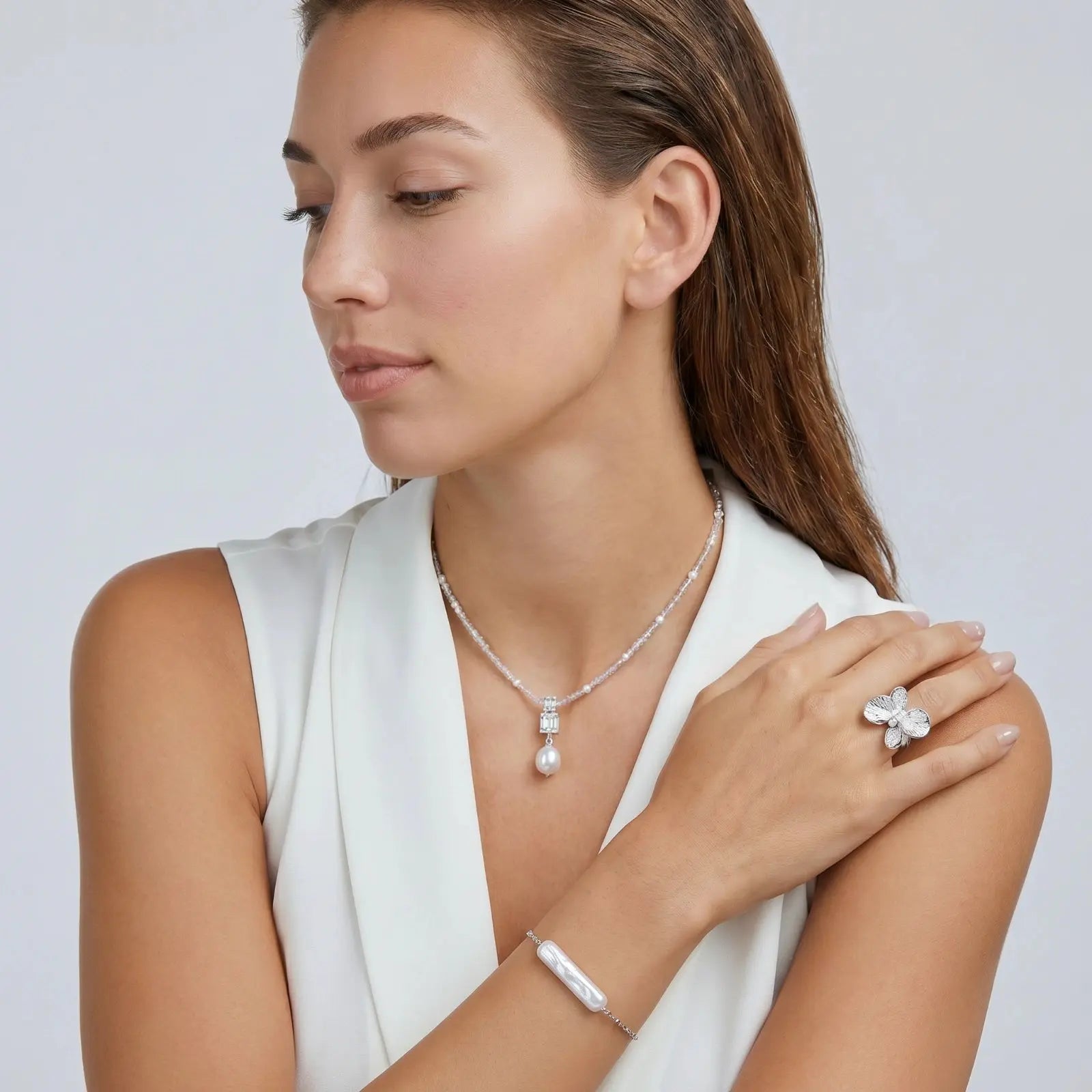 Woman wearing a necklace, ring, and bracelet on a plain background