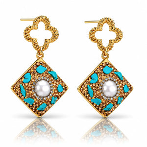 Pair of gold earrings with a diamond-shaped design and a central pearl on a white background
